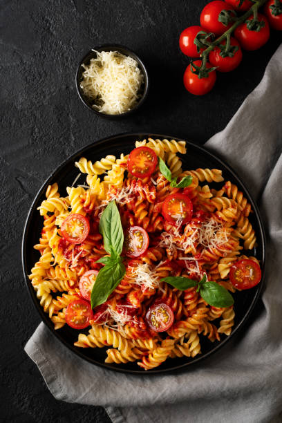 istock Fusilli pasta with tomatoes, basil, parmesan, and sauce on back background 1474888189
