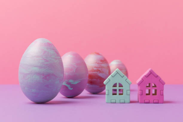 istock Easter eggs painted in fluid art technique and house models against pink background. Creative Easter holiday greeting concept 1474888459