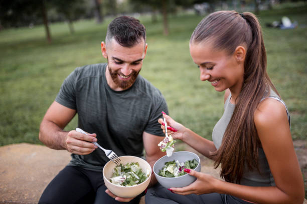 Happy sporty couple eating vegetable salad after intensive workout Happy sporty couple eating vegetable salad after intensive workout eating body building muscular build vegetable stock pictures, royalty-free photos & images