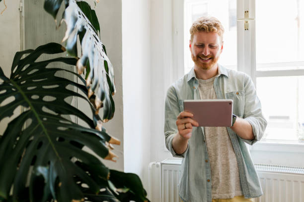 istock Cheerful ginger man  freelancer using digital tablet for social media, e-banking, mobile application, e-learning... 1474890859