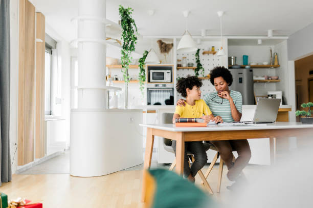istock Boy writing on a book while his mother working on laptop. Kid studying with mother working from home. 1474891029