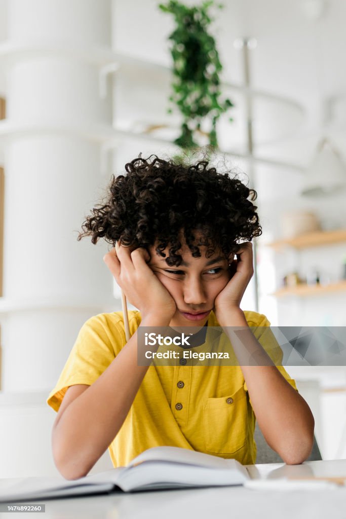 Sad tired frustrated boy sitting at the table with many books and doing homework. Learning difficulties, education concept Child Stock Photo