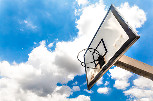 Canasta vieja de basketball vista desde abajo, cielo azul con nubes de fondo