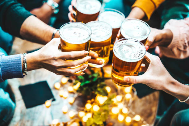 Group of people drinking beer at brewery pub restaurant - Happy friends enjoying happy hour sitting at bar table - Closeup image of brew glasses - Food and beverage lifestyle concept stock photo