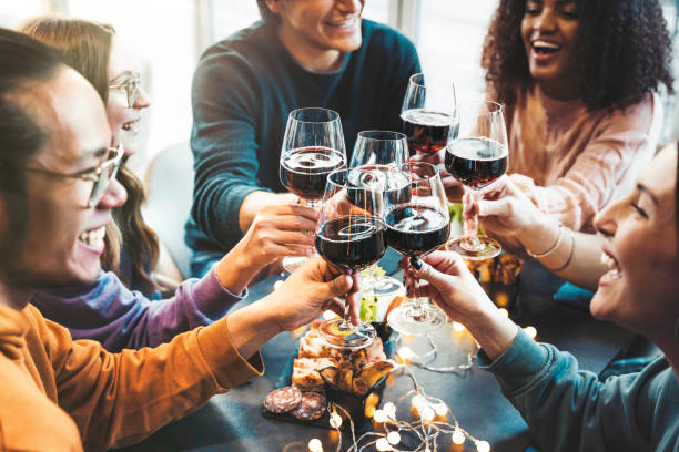 Multiracial group of friends toasting red wine sitting at bar restaurant table - Millennial people enjoying dinner party together - Life style concept with guys and girls hanging out on weekend stock photo