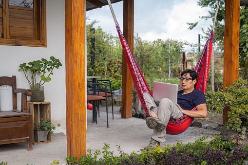 Man with glasses sitting in a hammock working with his computer in a garden. High quality photo
