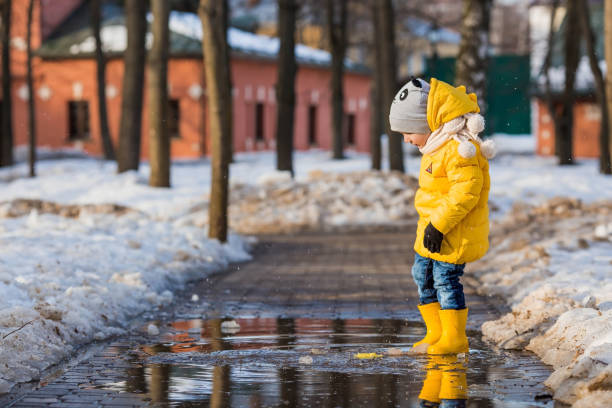 istock A small child in yellow rubber boots and a jacket runs through puddles, has fun, plays and launches paper boats. Spring break photo. It's springtime. 1474895127