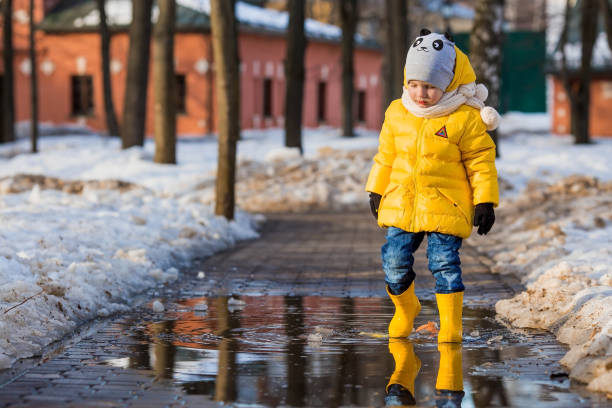 istock A small child in yellow rubber boots and a jacket runs through puddles, has fun, plays and launches paper boats. Spring break photo. It's springtime. 1474895131