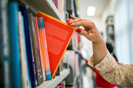 Woman's hand picking a book from a library bookshelf