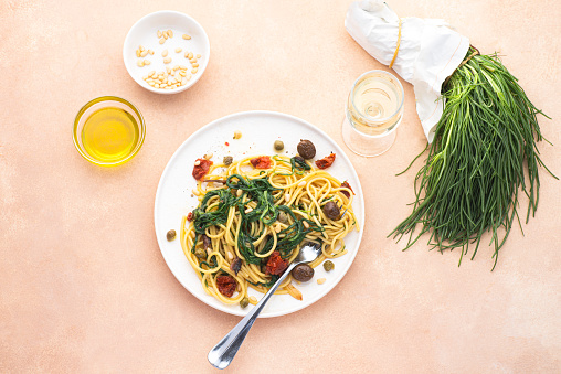 Spaghetti  with Italian Agretti, Barba di frate or Saltwort or  Salsola Soda, olives, anchovy, tomatoes, capers,  pine nuts and olive oil, spring Italian recipes. Pink soft spring background,  seasonal Italian cuisine, rare recipes