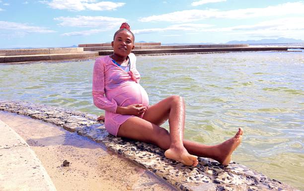 Young black African pregnant woman sitting on the beach