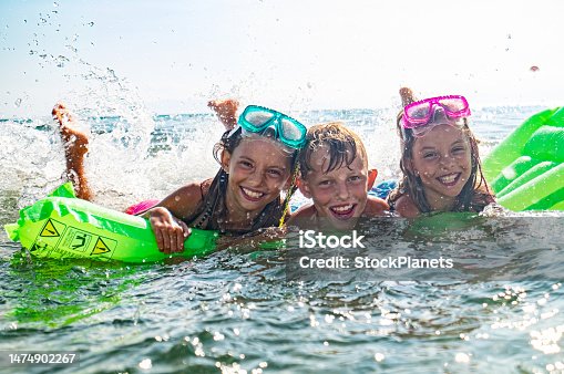 istock Girls and boys bathe together in the sea on a mattress. 1474902267