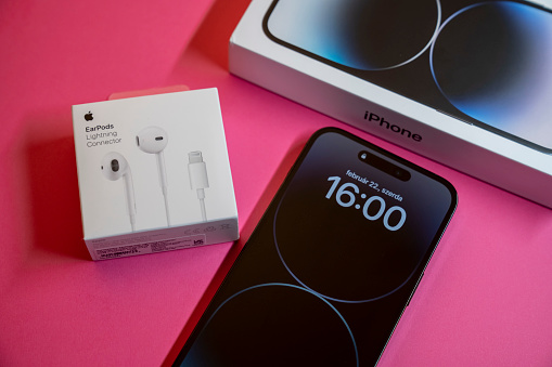 New iPhone 14 pro max and Apple Earpods, Airpods white earphones for listening to music and podcasts, in a closed box. Isolated pink background. Budapest, Hungary - February 16, 2023