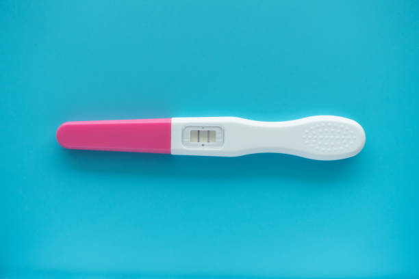 istock White Plastic Pregnancy test positive with two stripes results isolated on Pastel light blue background. Closeup. Top down view. 1474902643
