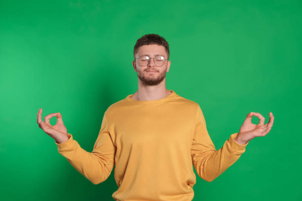 istock Young man meditating on green background. Zen concept 1474902979