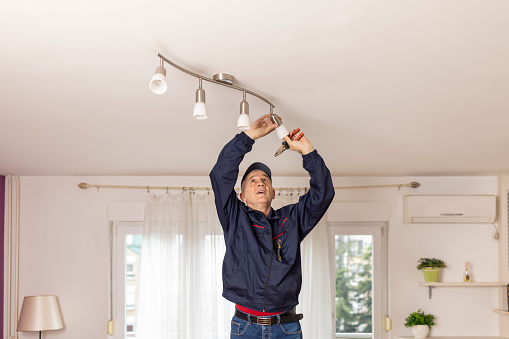 Man screws in light bulb in the chandelier. Mature man changing a ceiling energy saving light in living room