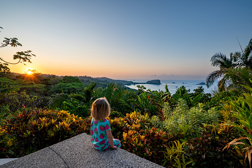 Toddler girl enjoying a vibrant sunrise over the wild untamed coastal beauty of Manuel Antonio National Park on the Pacific Coast of Costa Rica.