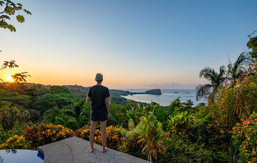 Woman enjoying a vibrant sunrise over the wild untamed coastal beauty of Manuel Antonio National Park on the Pacific Coast of Costa Rica.