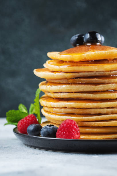istock Delicious pancakes, with fresh blueberries, raspberry and maple syrup or honey on a dark background 1474912436