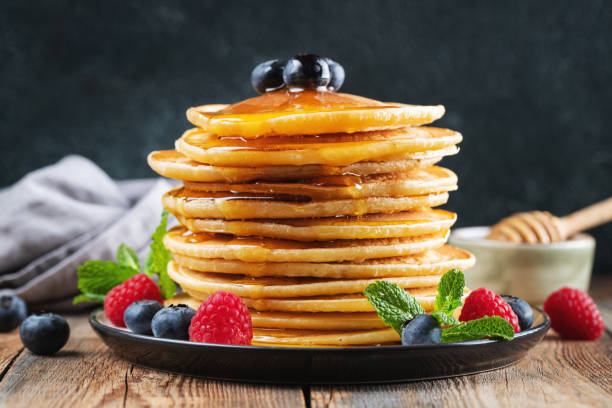 istock Delicious pancakes, with fresh blueberries, raspberry and maple syrup or honey on a dark background 1474912437
