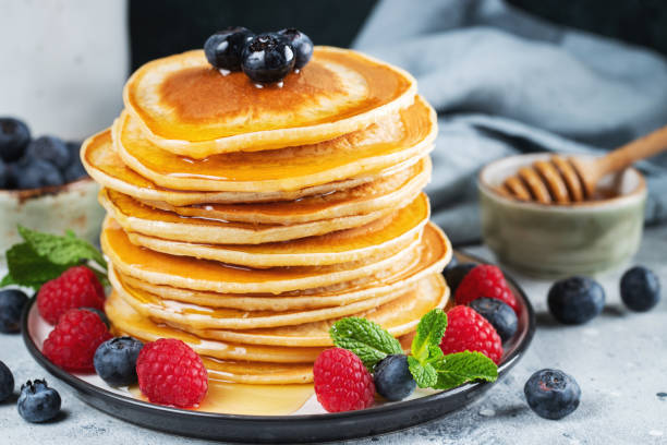 istock Delicious pancakes, with fresh blueberries, raspberry and maple syrup or honey on a dark background 1474912443