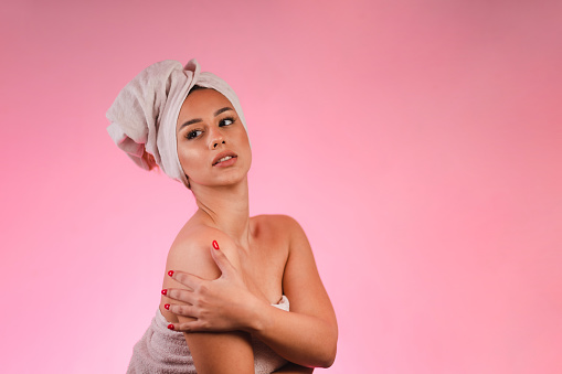 Studio portrait of a beautiful young woman wearing a towel while applying lotion to her body. Self care concept.