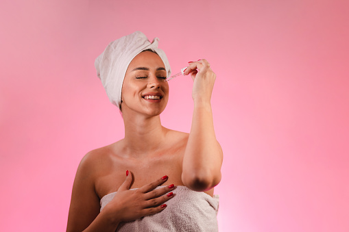 Studio portrait of a beautiful woman moisturizing her face. She is wearing towels.