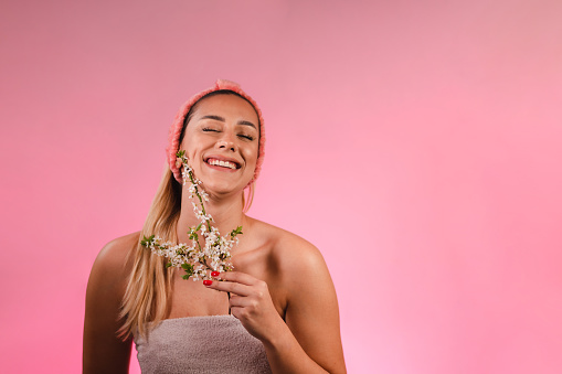 Studio shot of a beautiful young woman posing with a tree blossom while smiling.