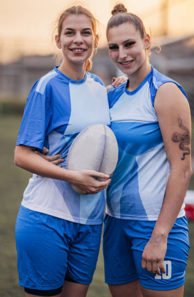 Two women, female rugby players on rugby field together outdoors.