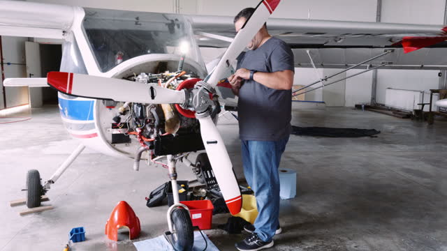 Aircraft mechanic repairs airplane engine in airport hangar.