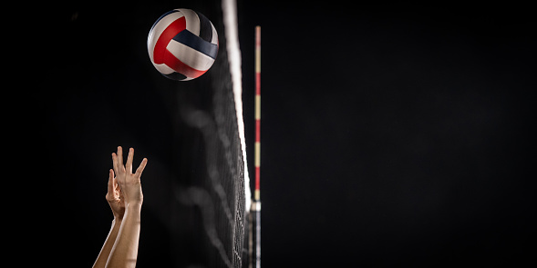 A red, white and blue size 5 beach volleyball is in the air, near an outdoor net. At 100% there is some sand visible flying around the ball.