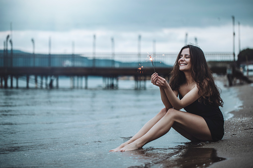 beautiful woman with sparkler in hand is sitting on the beach
