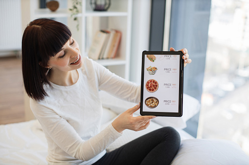 Portrait of adorable woman showing digital tablet with website of fast food selling with discount on screen. Ecommerce, online shopping and modern gadgets concept.
