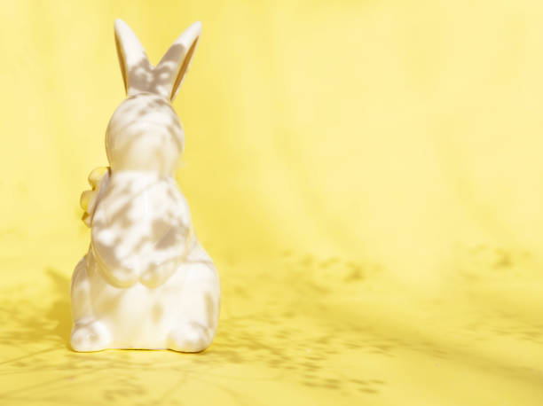 Easter minimalistic background with a ceramic rabbit and a shadow of flowers on it. Sunlight with a sharp shadow. Creative concept of Happy Easter. Flat position, space for text.