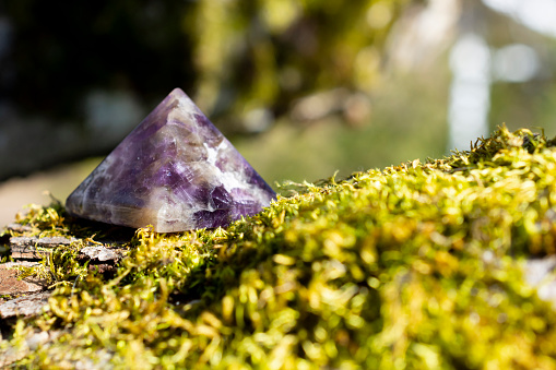 A close up image of a amethyst crystal pyramid on a thick green patch of moss.