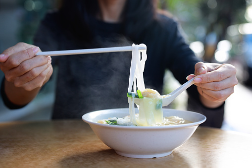 Cropped shot of an Asian woman enjoying shrimp wontons soup noodle at hawker stall