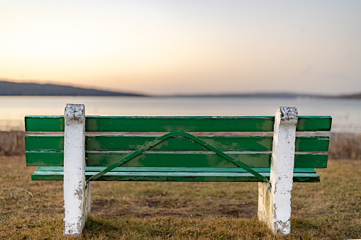 Green wood bench from behind with lake background
