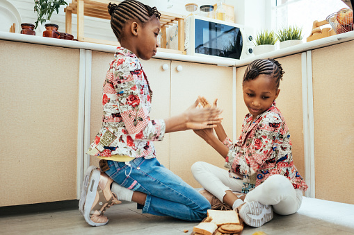 Twin African girls playing rock paper scissors in kitchen room