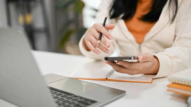 istock Cropped image of an Asian woman using her phone while working at her desk. 1474940919