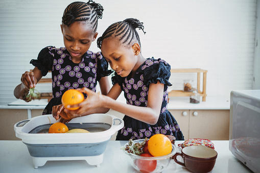 Twin girls washing orange fruit in the kitchen