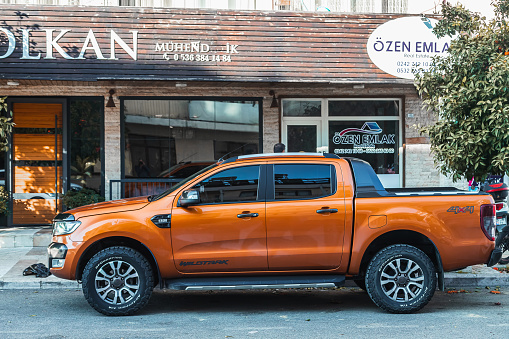 Side , Turkey -  January  31,  2023:      orange pickup Ford Ranger is parked  on the street on a warm day against the backdrop of a shop , garden