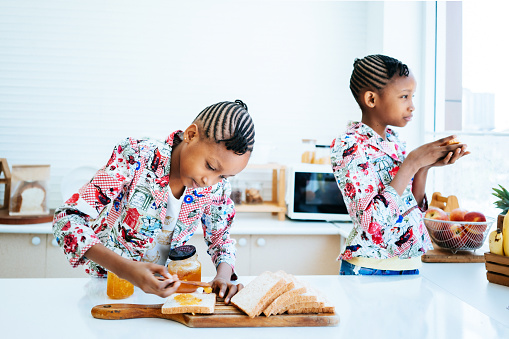 Twin African girls eating toasted bread in morning at home