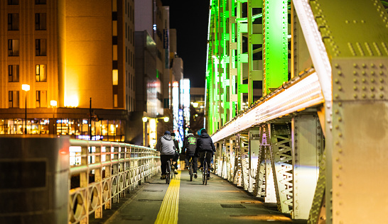 18 March 2023, Morioka City, Iwate. A group of teenagers riding their bikes together across a bridge in the city.