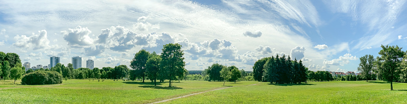 wide panoramic view of green park near city residential area on sunny summer day.