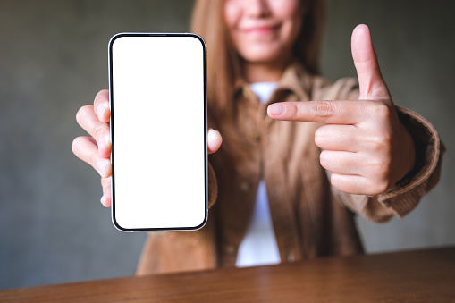 Mockup image of a young woman holding, showing and pointing finger at a mobile phone with blank white screen
