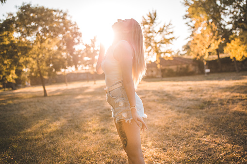 Beautiful blonde woman enjoying nature and sunset while standing in park during summer day