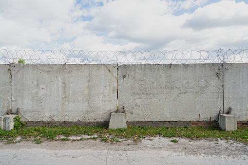 Concrete fence with metal barb construction on blue sky background.