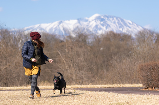 A mid age Japanese woman running with her dog in a public park.