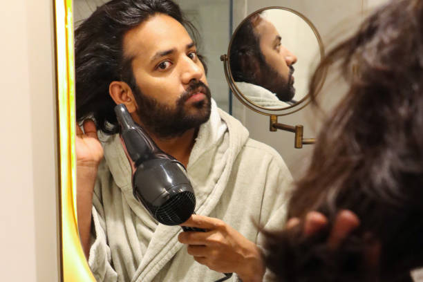 istock Image of reflection in mirror of Indian man stood at sink bathroom wearing bathrobe using hair dryer after having a shower, self care and grooming concept 1474962317