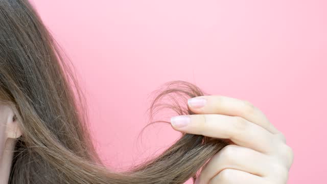 Girl holding her hair with split ends close-up on pink background.